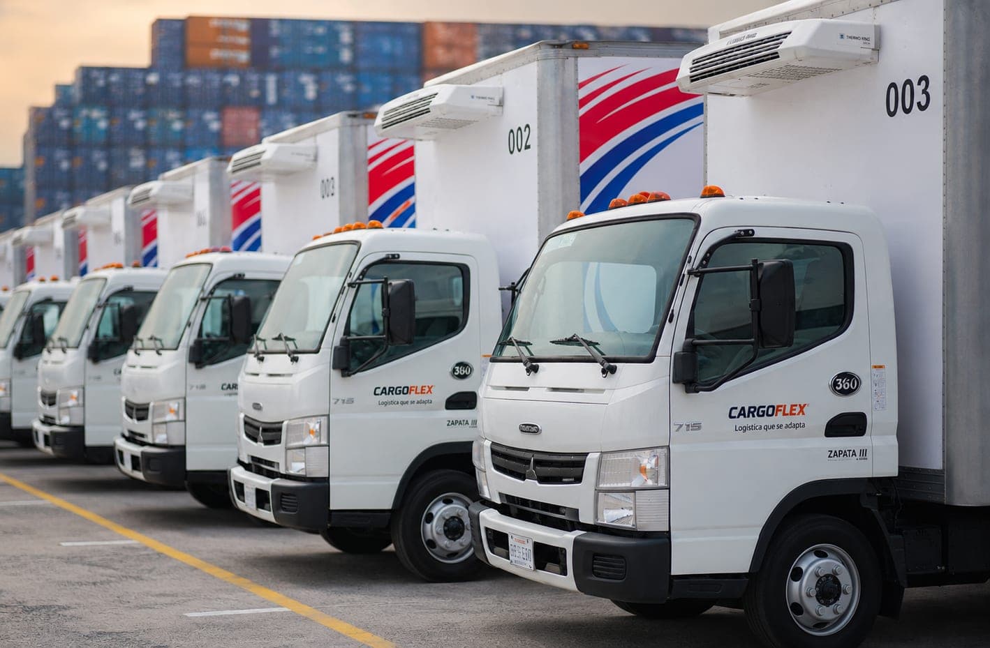 Flota de camiones de caja rotulados de CargoFlex formados frente a contenedores en Monterrey